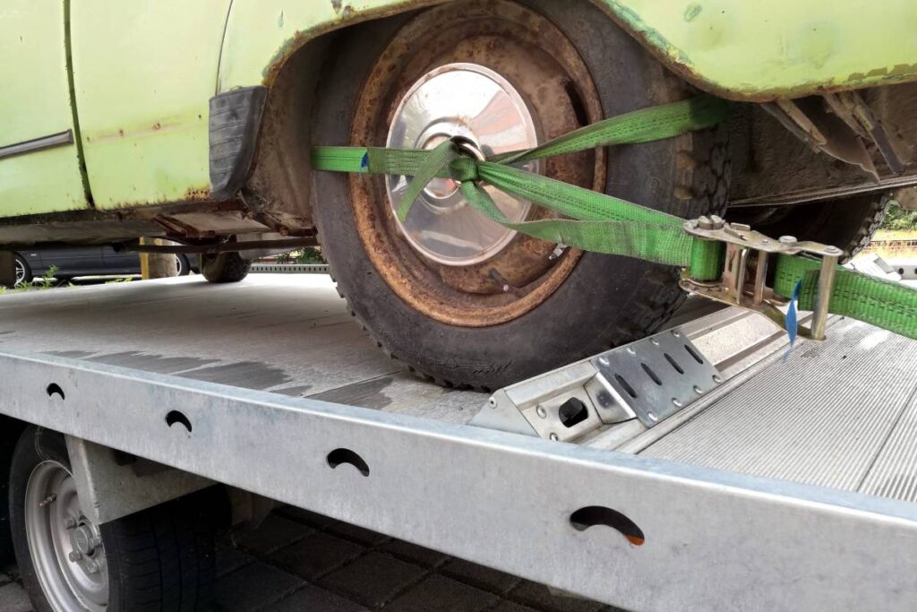 An old and green crashed car being taken for repairing  on a truck